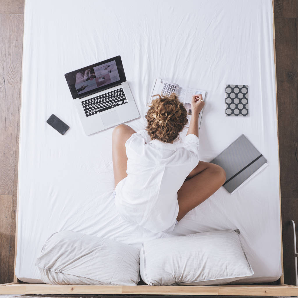 Сверху фотография женщины, работающей на ноутбуке и сидящей на кровати
. - Фото, изображение