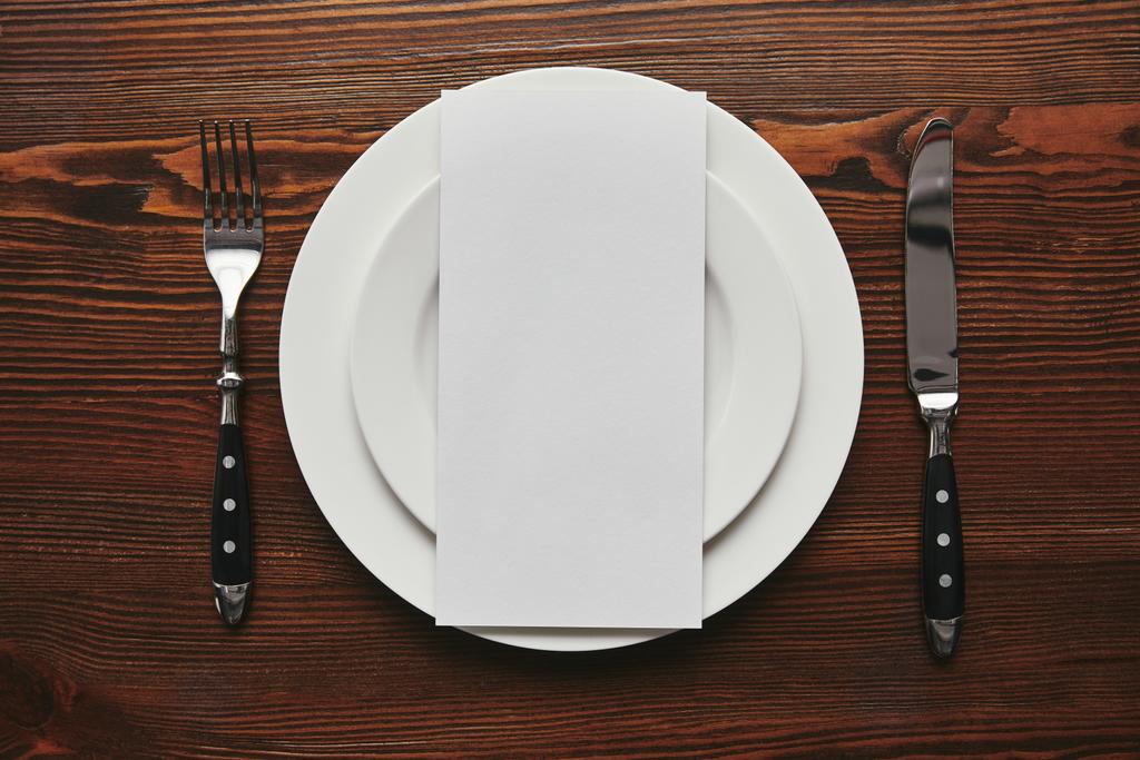 вид зверху порожня листівка на білих тарілках з виделкою і ножем на дерев'яному столі
  - Фото, зображення