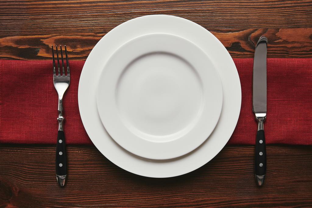 vista superior de platos blancos vacíos redondos con tenedor y cuchillo sobre mesa de madera
  - Foto, Imagen