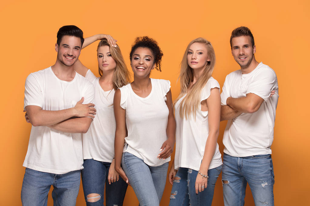 Pięć młodych multi etnicznych ludzi uśmiecha się do kamery, pozowanie na tle pomarańczowy studio w białe koszule. - Zdjęcie, obraz