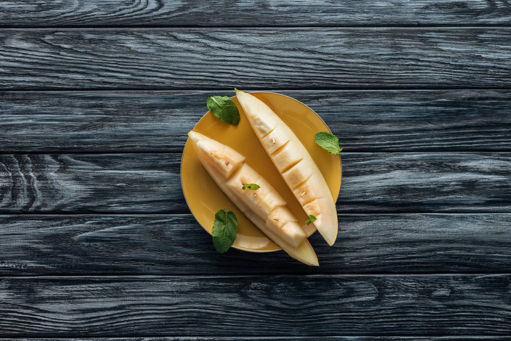 bovenaanzicht van verse rijpe zoete meloen gesneden op gele plaat op houten oppervlak  - Foto, afbeelding