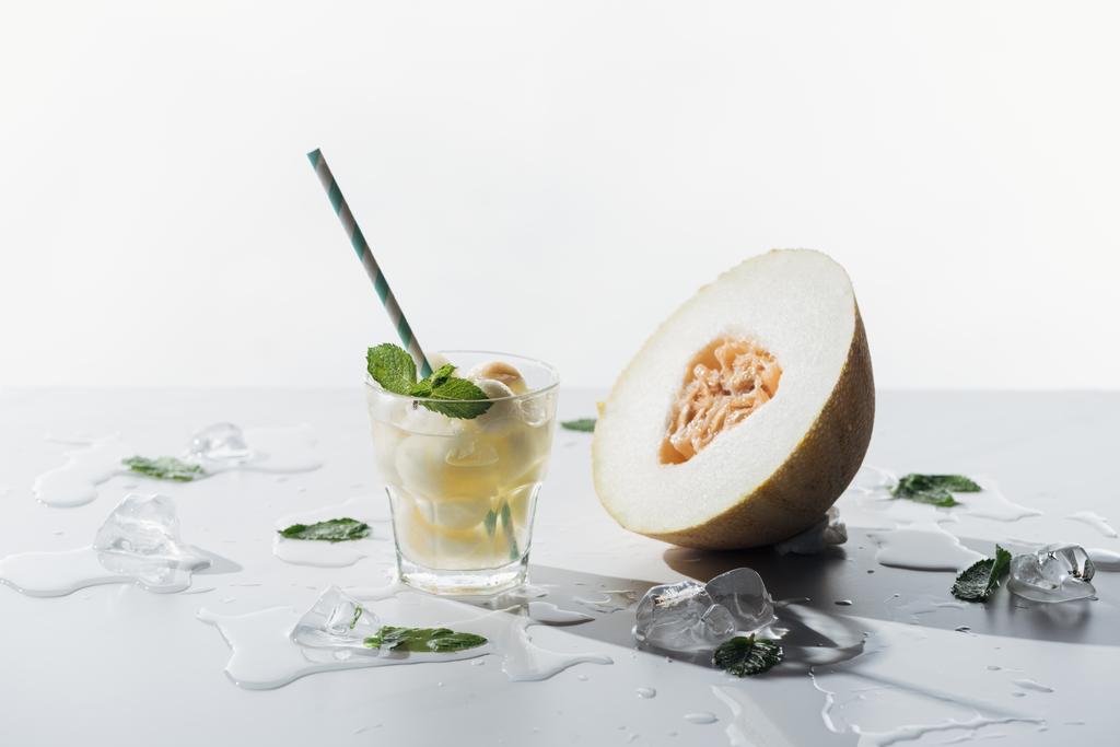 delicious summer drink with mint and melon in glass, melted ice cubes and half of ripe melon on white   - Photo, Image