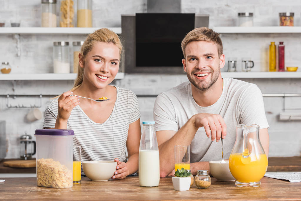smiling couple looking at camera and having breakfast in kitchen - Photo, Image
