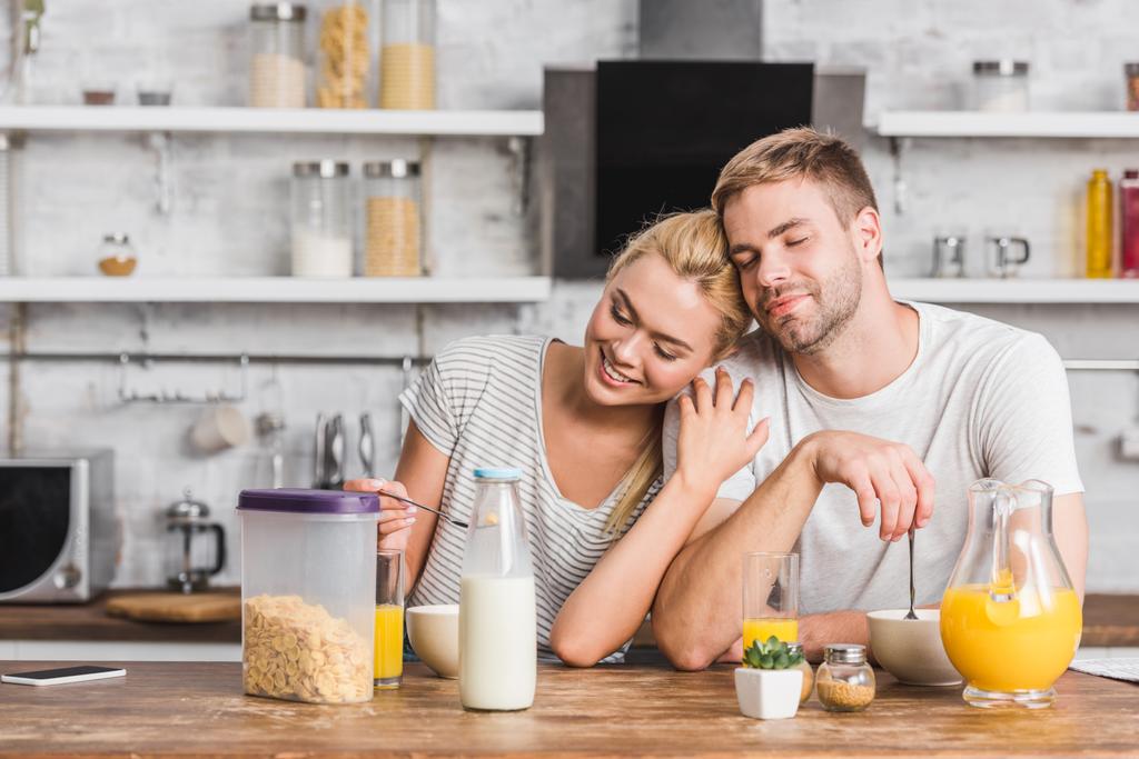 Paar frühstückt und umarmt sich mit geschlossenen Augen in Küche - Foto, Bild