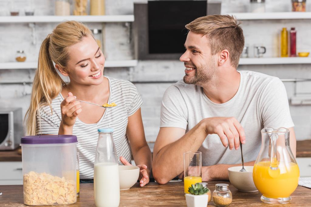sonriente pareja comiendo copos de maíz con leche en el desayuno en la cocina
 - Foto, imagen
