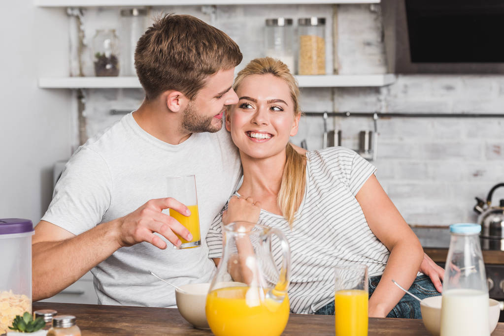 счастливый парень обнимает подругу во время завтрака на кухне, и они смотрят друг на друга
 - Фото, изображение