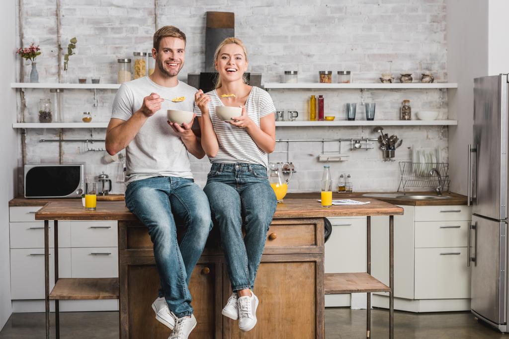 happy couple having breakfast and sitting on kitchen counter - Photo, Image