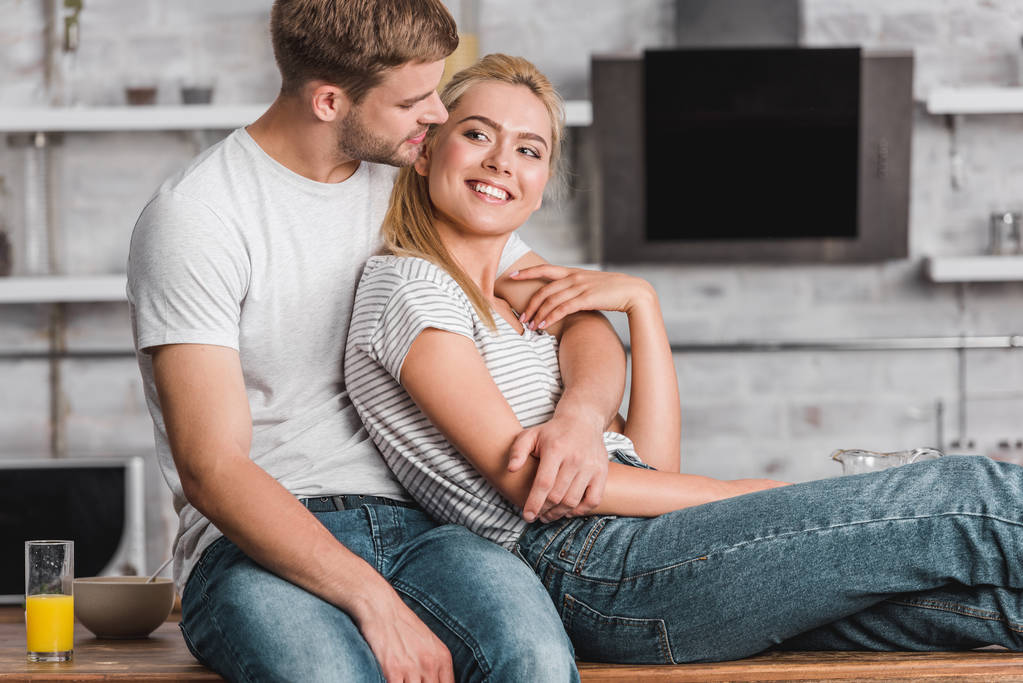 smiling couple hugging and sitting on kitchen counter - Photo, Image