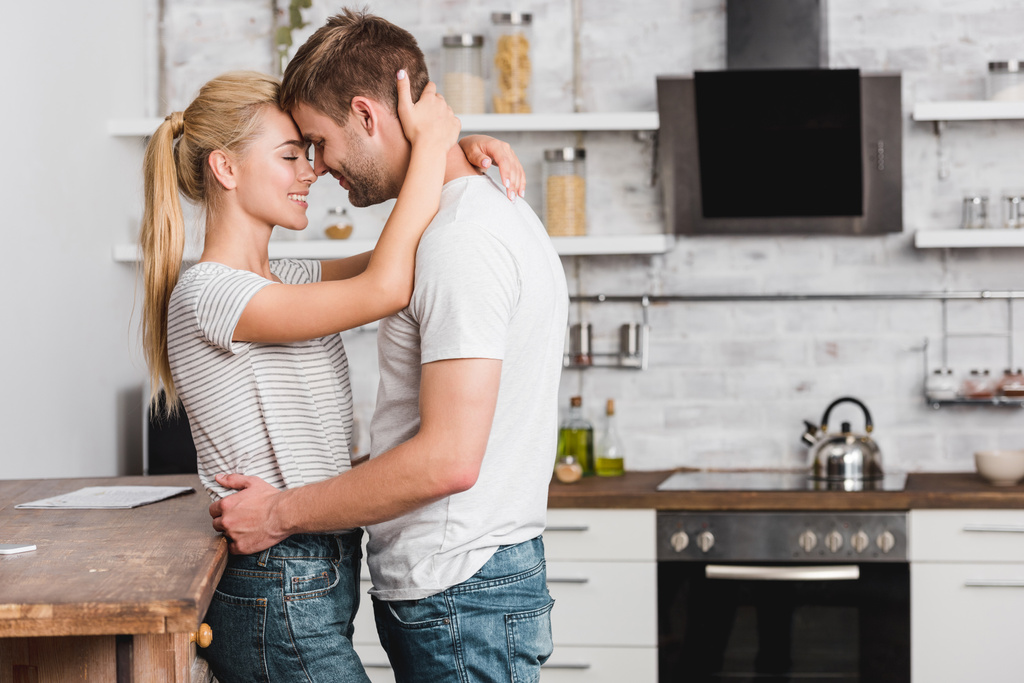 Μερική άποψη του ζευγάρι αγκαλιά στην κουζίνα και να ακουμπά στο πάγκο της κουζίνας - Φωτογραφία, εικόνα