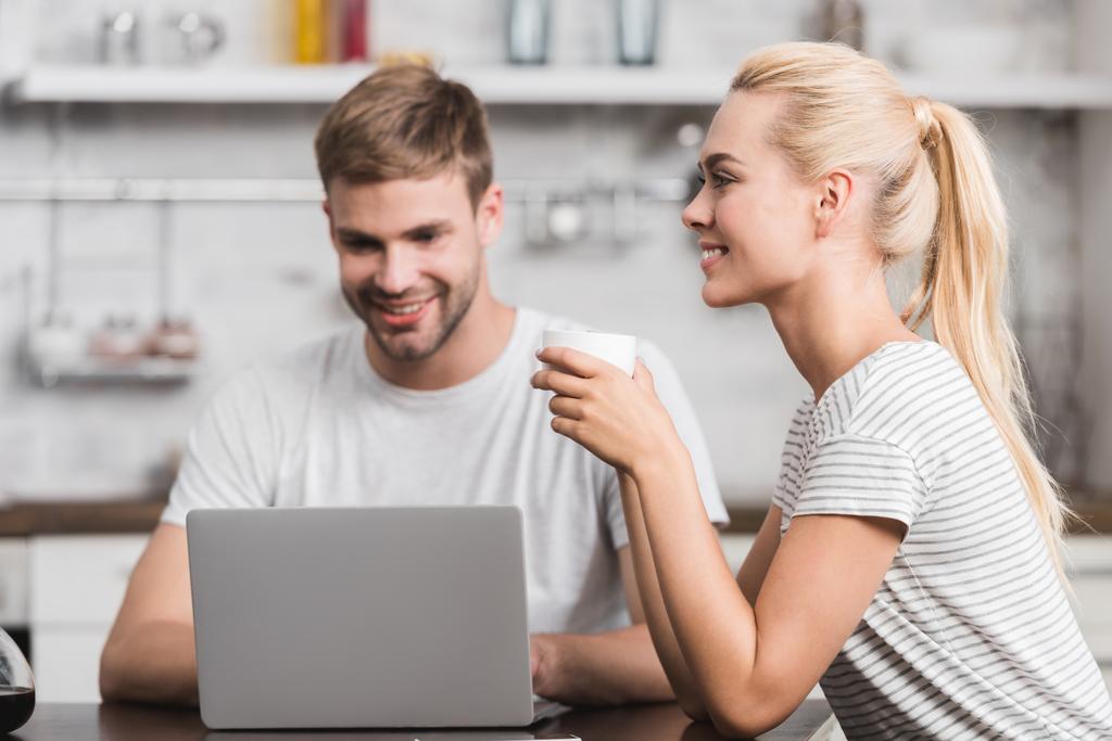 sorridente giovane uomo utilizzando il computer portatile mentre felice ragazza bere caffè
 - Foto, immagini