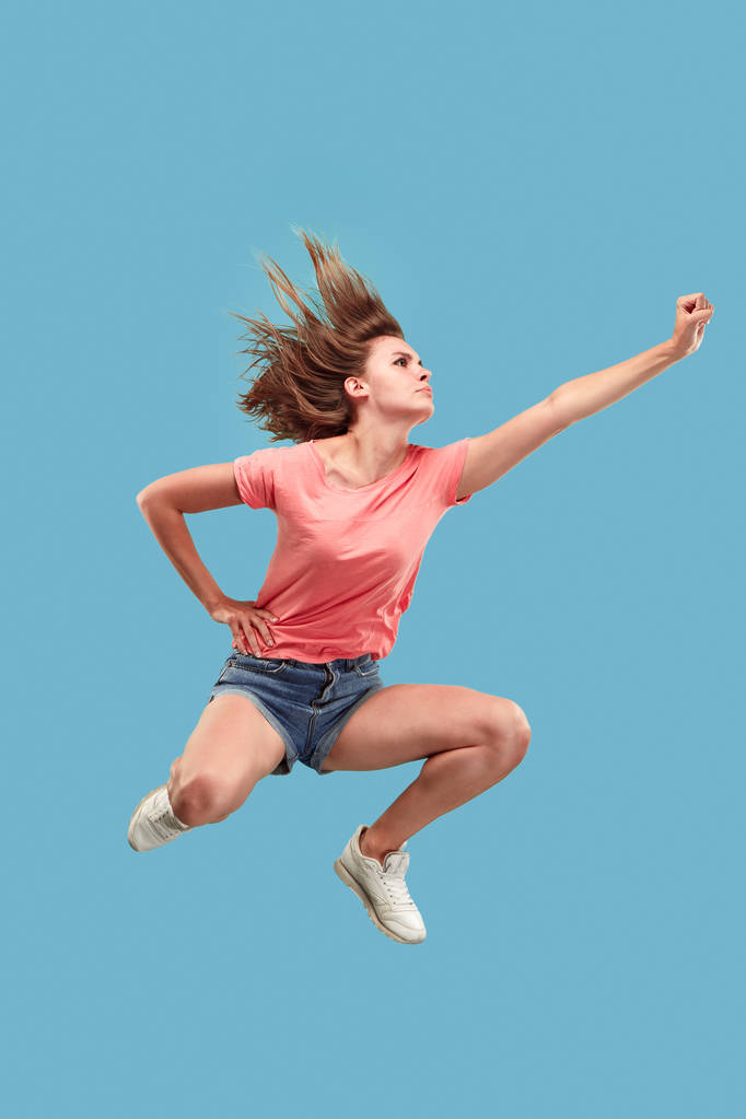 Libertad de movimiento. Mujer bastante joven saltando sobre fondo azul
 - Foto, Imagen