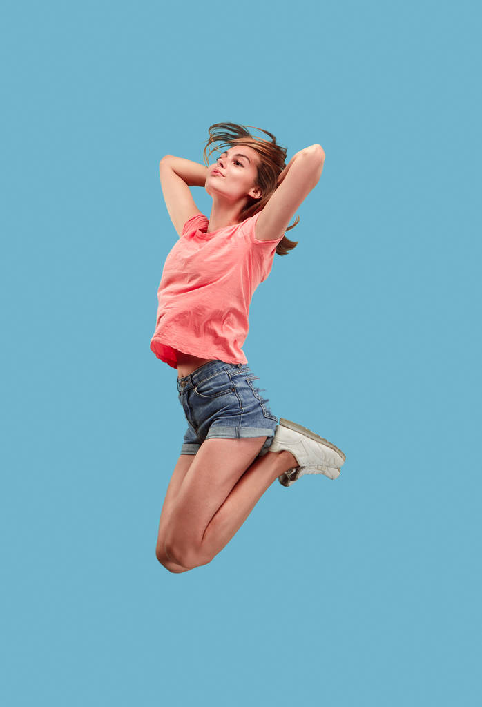 移動の自由。かなり若い女性が青い背景にジャンプ - 写真・画像