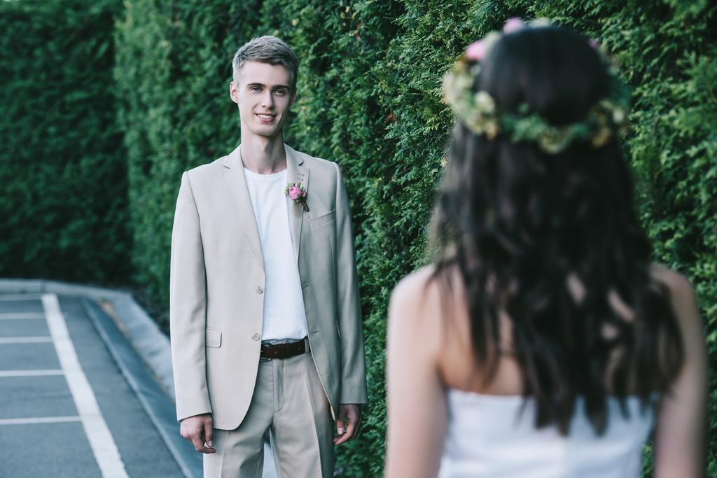 Selektivní fokus usměvavý pohledný ženich při pohledu na mladé nevěsty - Fotografie, Obrázek