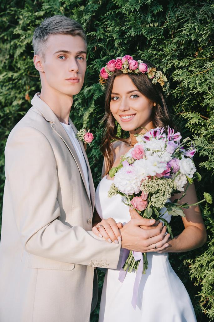 элегантная свадебная пара с цветочным букетом, смотрящая в камеру
 - Фото, изображение