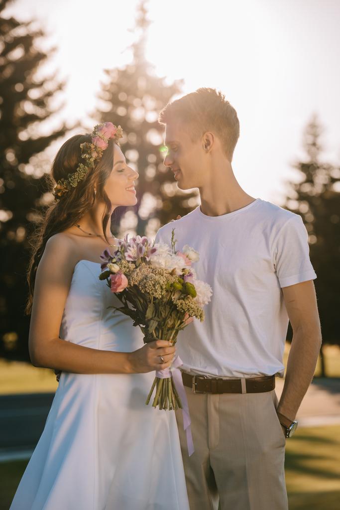 elegante bruidspaar met boeket lacht om elkaar - Foto, afbeelding