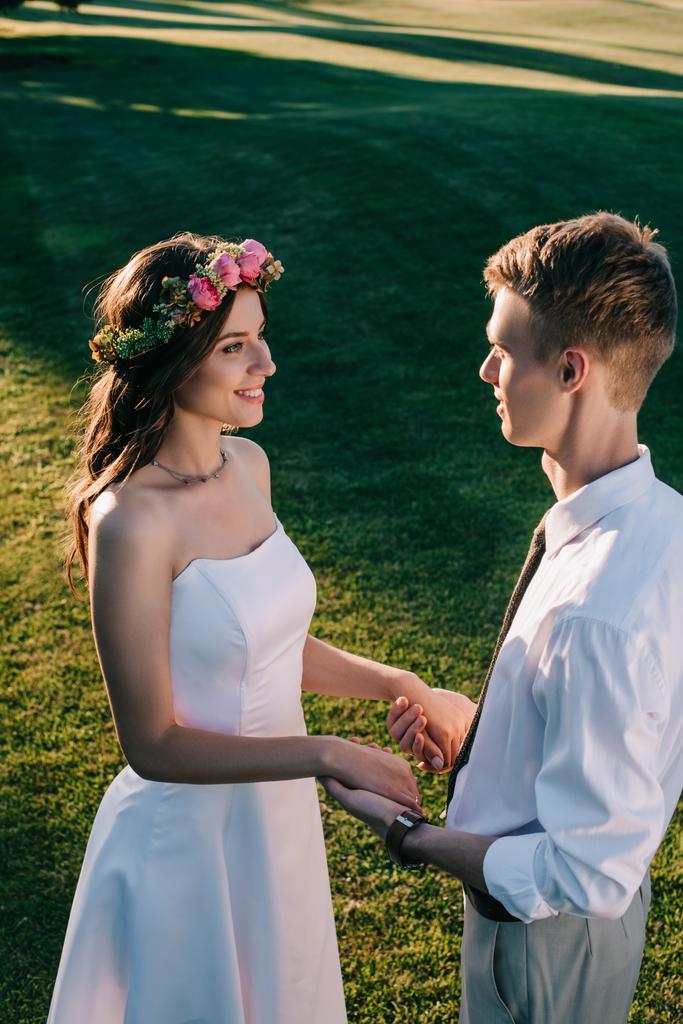 high angle view of beautiful young wedding couple holding hands and smiling each other in park  - Photo, Image