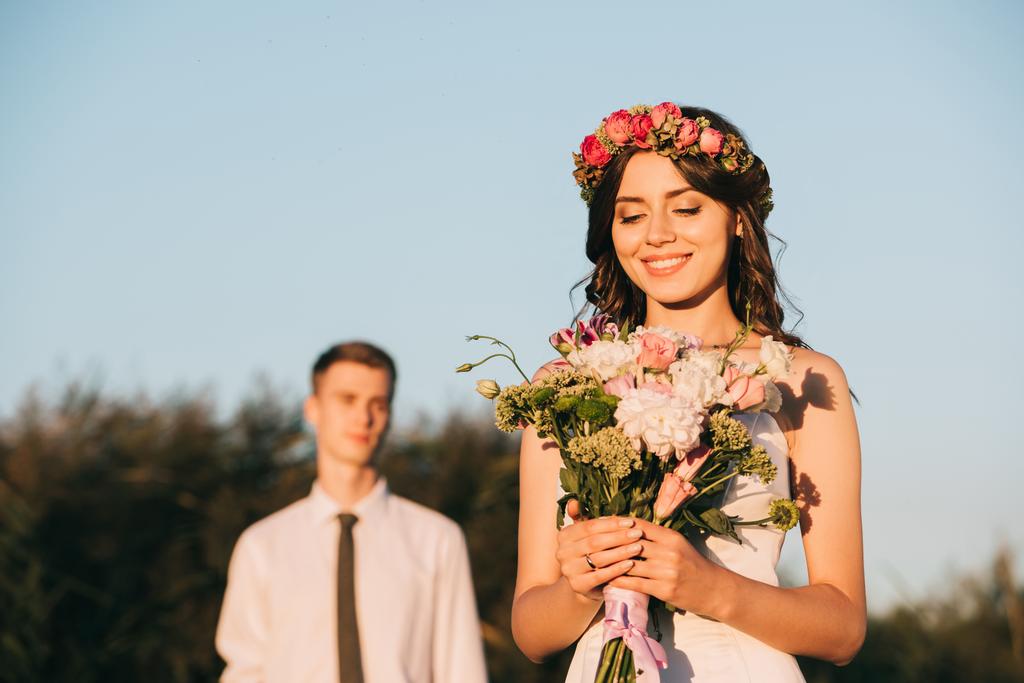 hermosa feliz joven novia celebración de ramo de boda y novio de pie detrás
 - Foto, imagen