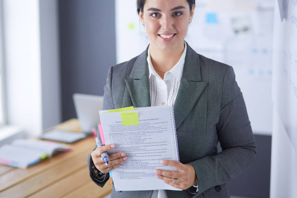 Mladá usměvavá žena stojí a drží knihu v úřadu - Fotografie, Obrázek