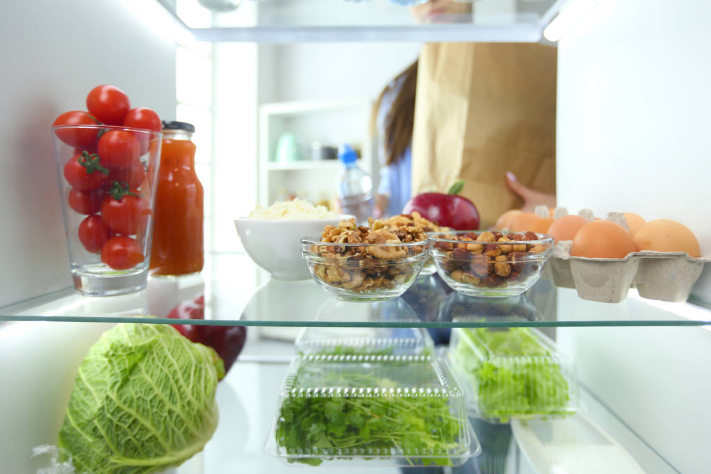Porträt einer Frau, die neben einem offenen Kühlschrank voller gesunder Lebensmittel, Gemüse und Obst steht. - Foto, Bild