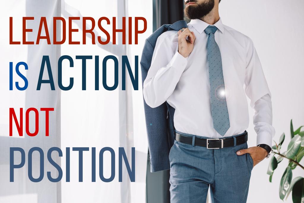 cropped view of businessman holding jacket and standing near window with "leadership is action not position" lettering - Photo, Image