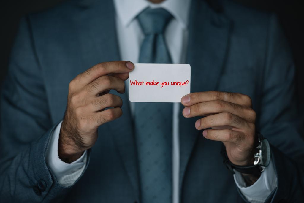 περικοπεί άποψη του επιχειρηματία στο κοστούμι εκμετάλλευση επαγγελματική κάρτα με την επιγραφή «Τι σας κάνει να μοναδική;» - Φωτογραφία, εικόνα