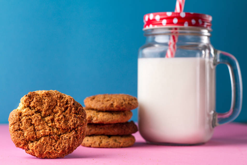 Healthy milk in glass jar and cookies on the pink table and on the blue background - Photo, Image