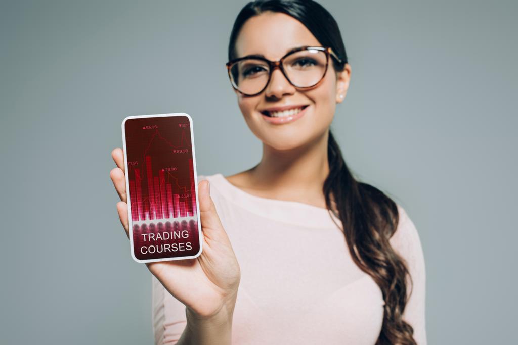 жінка показує смартфон з торговими курсами, ізольовані на сірому
 - Фото, зображення