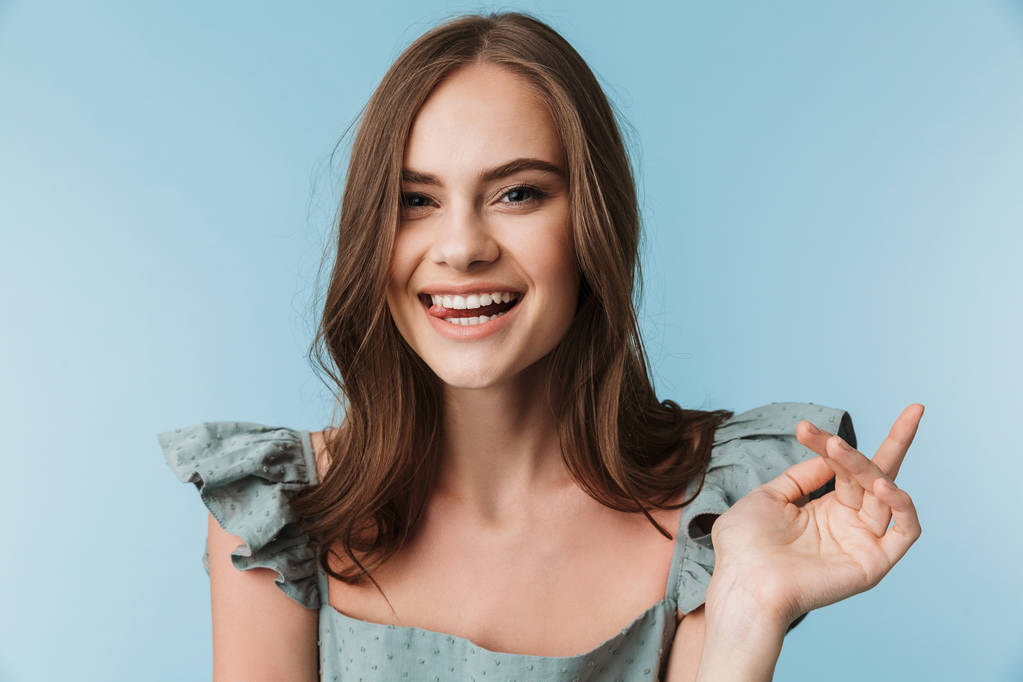 Image de jeune femme heureuse montrant la langue debout isolé sur fond bleu regardant caméra
. - Photo, image