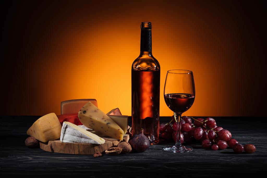 different types of cheeses, wine bottle and grapes on table on orange - Photo, Image