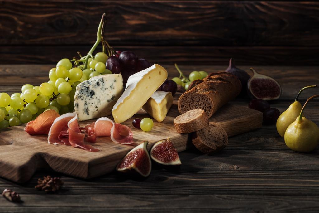 différents types de fromages, prosciutto et baguette sur planche à découper
 - Photo, image