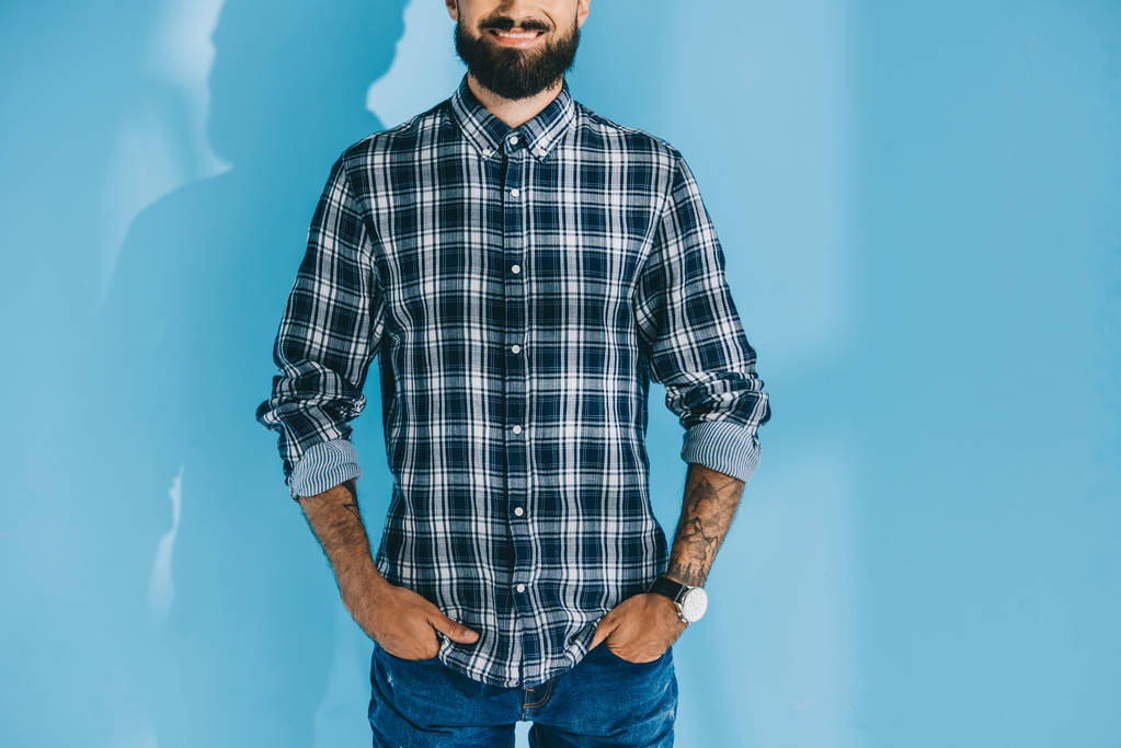 обрезанный вид бородатого человека, стоящего с руками в карманах, на голубом
  - Фото, изображение