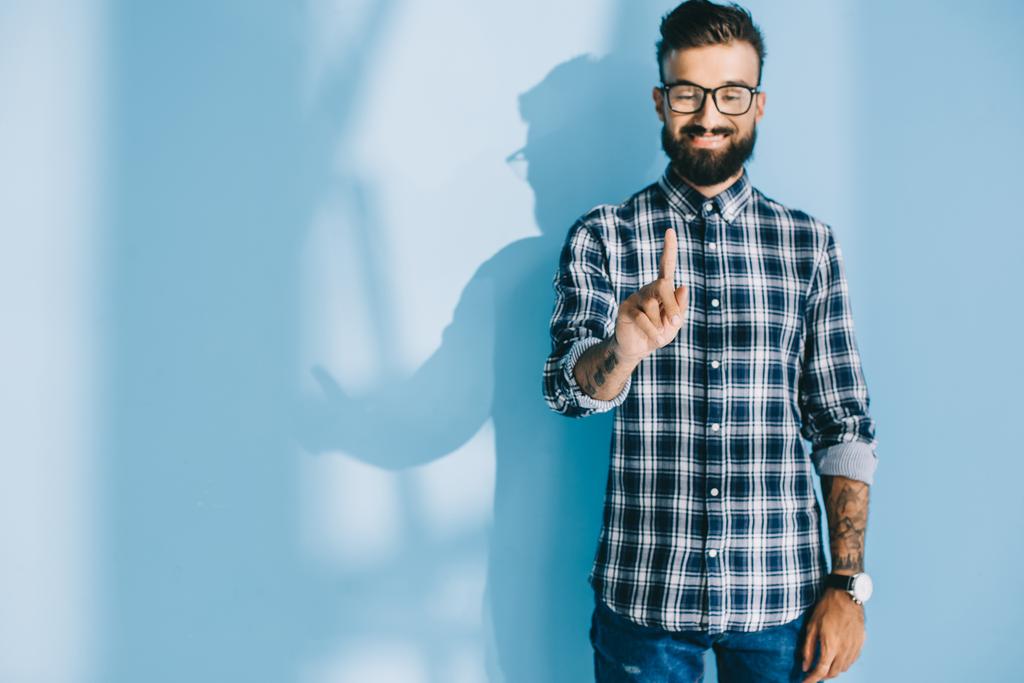 hombre barbudo sonriente con camisa a cuadros apuntando a algo, en azul
 - Foto, imagen