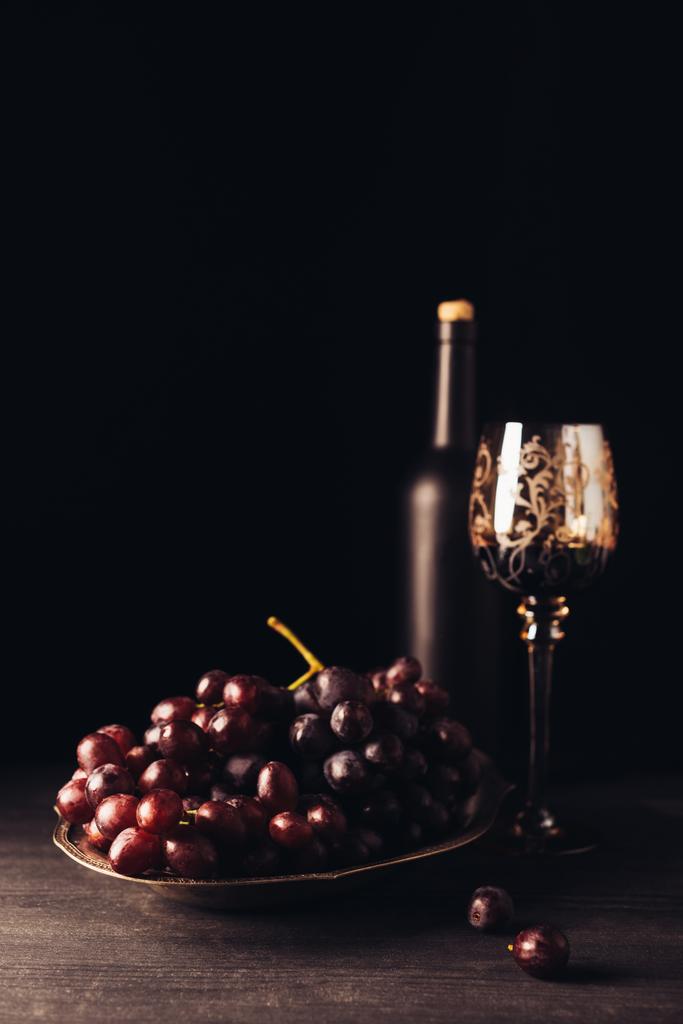 tuoreet kypsät rypäleet, lasi ja pullo viiniä puupöydällä mustalla
 - Valokuva, kuva