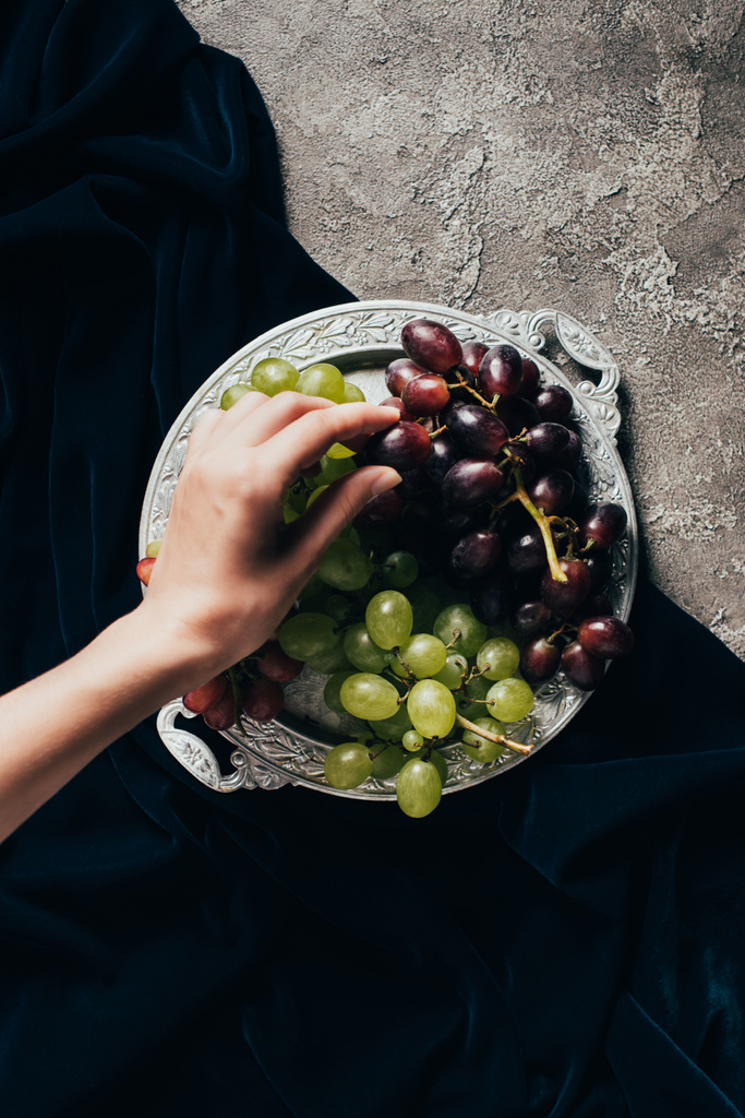 vista superior parcial de pessoa comendo uvas deliciosas do prato vintage
 - Foto, Imagem