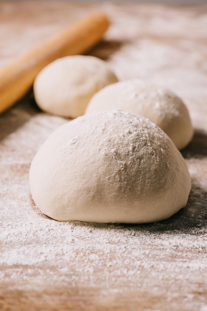 selective focus of raw dough for pizza and rolling pin on tabletop - Photo, Image