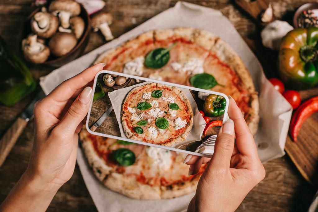 Plan recadré du blogueur alimentaire prenant une photo de pizza cuite sur du papier cuisson sur une surface en bois
 - Photo, image