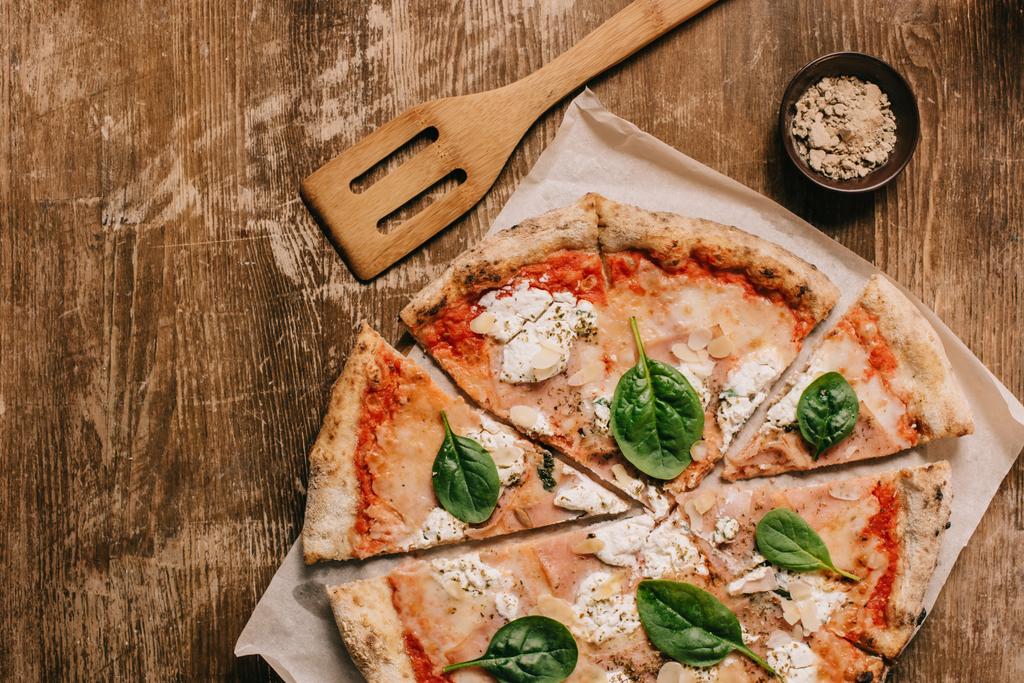 top view of cut italian pizza and wooden spatula on wooden tabletop - Photo, Image