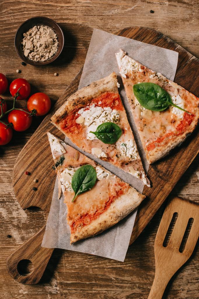 вид сверху на вырезанную итальянскую пиццу на доске для резки на деревянном столе
 - Фото, изображение