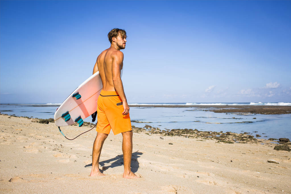 jovem surfista com prancha de surf em pé na praia de areia no dia de verão
 - Foto, Imagem