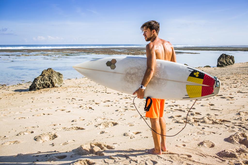 vista lateral del joven surfista con tabla de surf de pie en la playa de arena en el día de verano
 - Foto, Imagen
