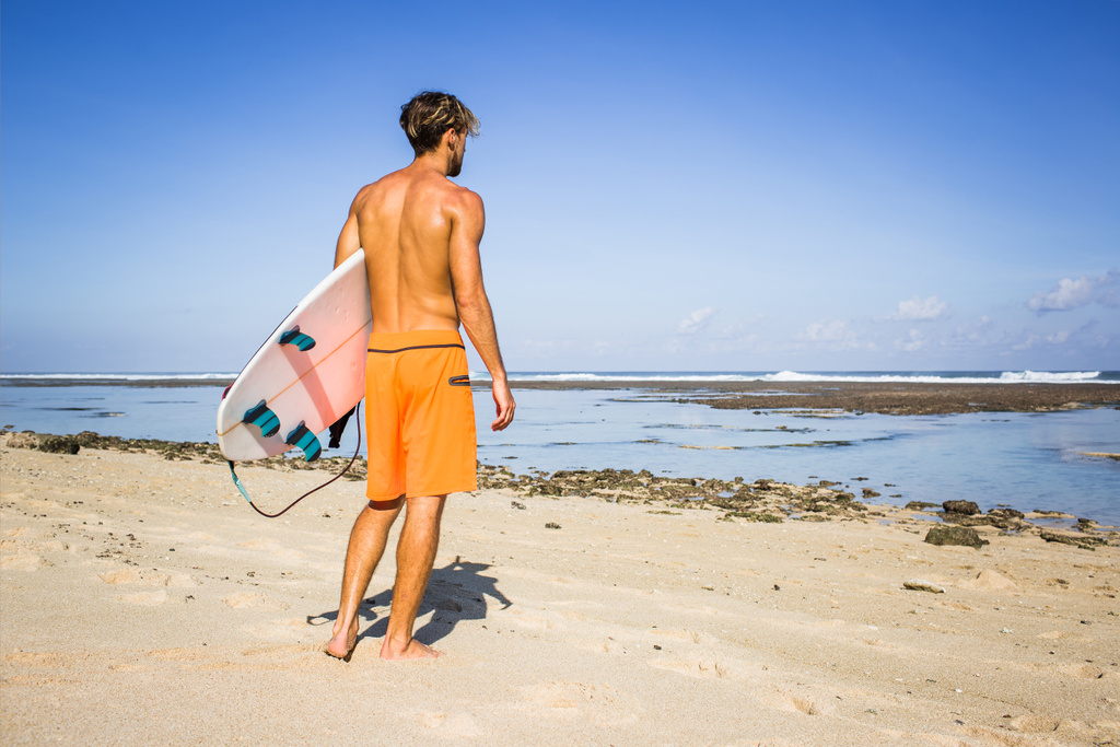 vista trasera del surfista con tabla de surf de pie en la playa de arena en el día de verano
 - Foto, Imagen