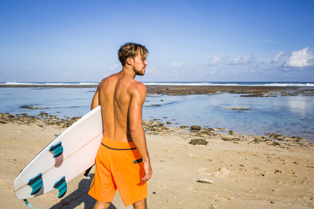 zadní pohled na surfař s surfování stojí na písečné pláži v letním dni - Fotografie, Obrázek