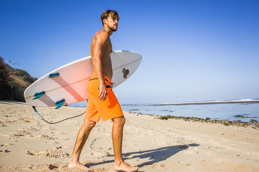 vue latérale du jeune sportif avec planche de surf marchant sur une plage de sable
  - Photo, image
