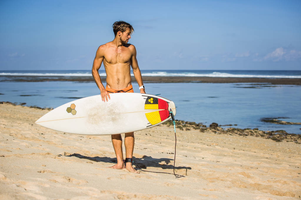 Nuori mies surffilauta hiekkarannalla lähellä merta
 - Valokuva, kuva