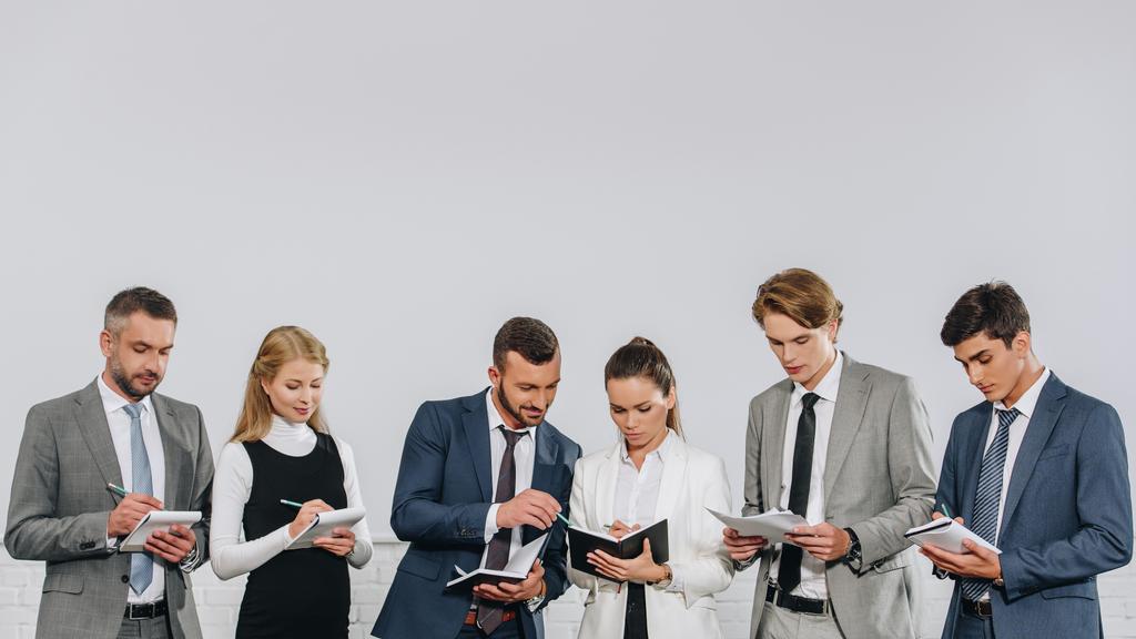 biznesmeni w formalnej nosić stojących w rzędzie i coś pisze do notebooków, podczas szkolenia w centrum - Zdjęcie, obraz