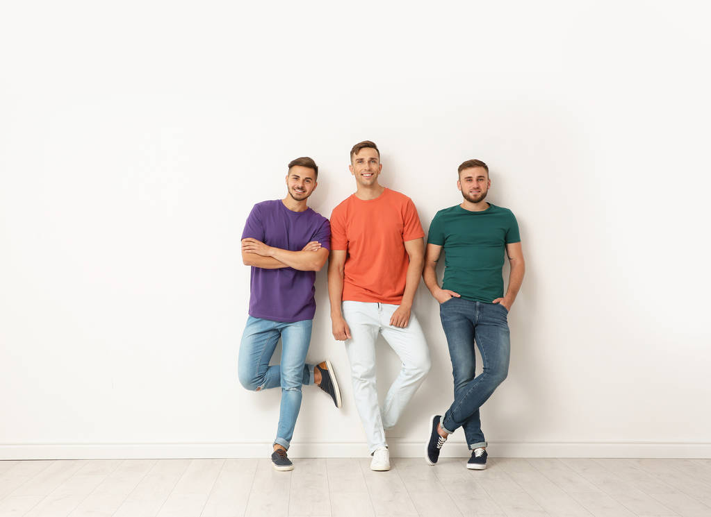 Grupo de jovens em jeans e camisetas coloridas perto de parede leve
 - Foto, Imagem
