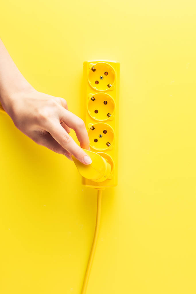 bijgesneden shot van een persoon invoegen plug in de wandcontactdoos op geel - Foto, afbeelding