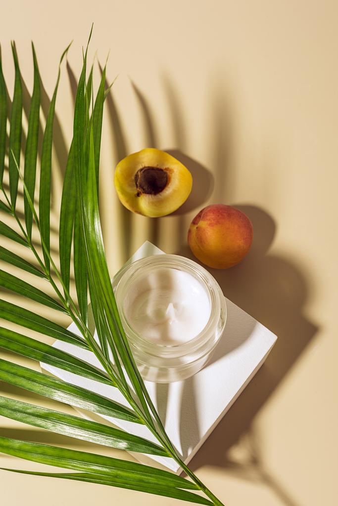 vue du haut de la crème corporelle, des abricots et de la feuille de palme verte sur fond beige
 - Photo, image
