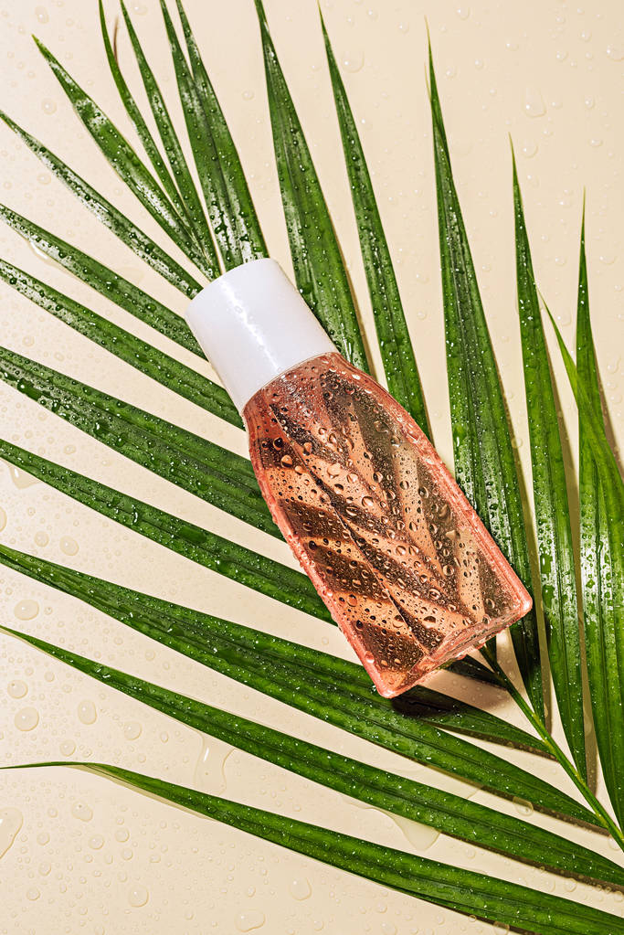 top view of micellar water on green palm leaf with water drops on beige background - Photo, Image