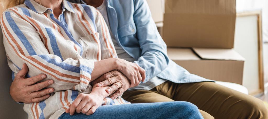 partial view of senior couple holding hands and sitting together on couch in new house  - Photo, Image